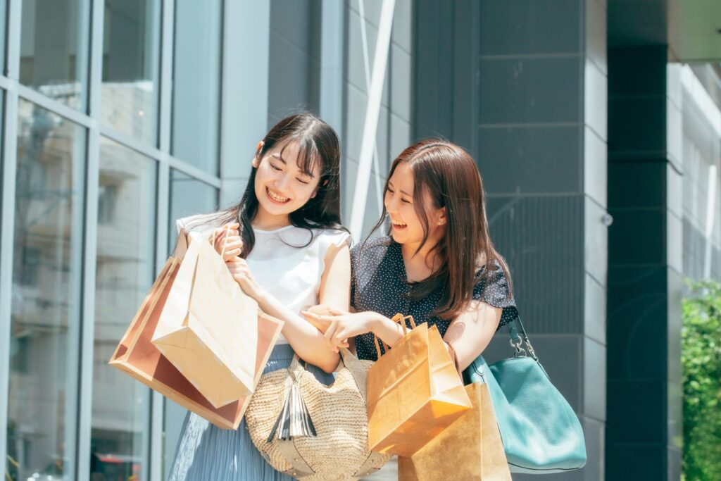 Two friends strolling past shops with shopping bags